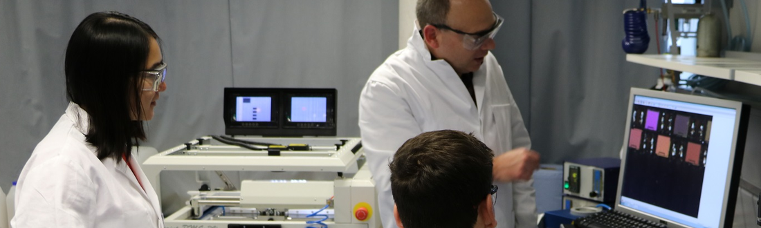 Drei Wissenschaftler in weißen Kitteln blicken im Labor auf einen Bildschirm